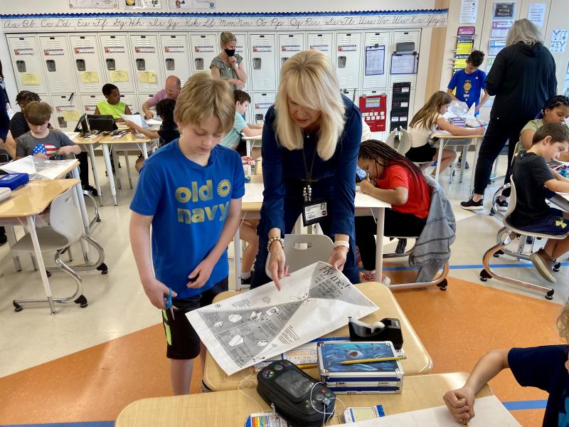 Parent volunteer Kristin Lamb helps Tyler Burleson cut out his kite.